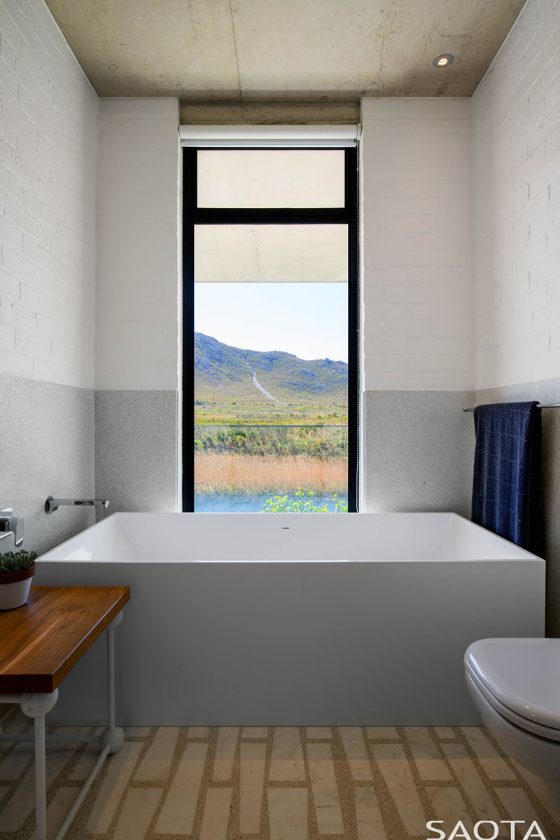 In this modern bathroom, the bathtub sits at one end of the room and a vertical window frames the view like artwork. #ModernBathroom #BathroomDesign