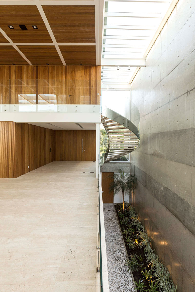 Stepping inside this modern house, there's an open hallway with a view of the stairs that lead to the upper floor, and a view of the large concrete wall found at the side of the house. #Stairs #Skylights #ModernHouse