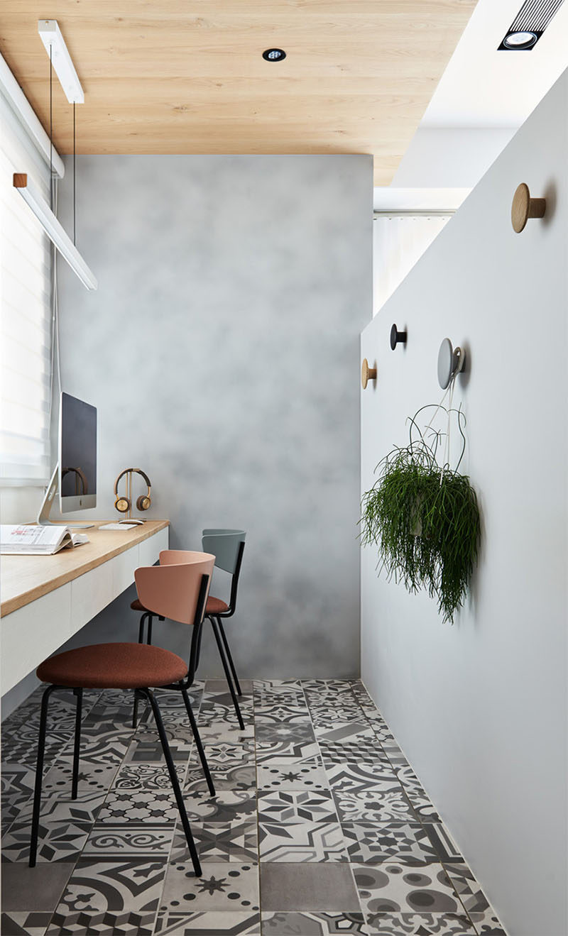 Hidden behind a pony wall in the living room of this apartment is a home office. Patterned tiles cover the floor while a wood ceiling adds warmth to the space. #HomeOffice #InteriorDesign