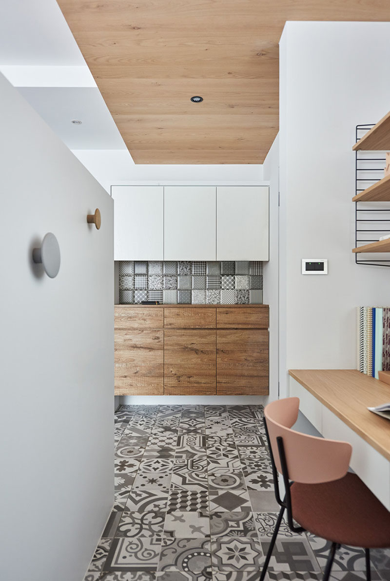 Hidden behind a pony wall in the living room of this apartment is a small home office. Patterned tiles cover the floor while a wood ceiling adds warmth to the space. #HomeOffice #InteriorDesign