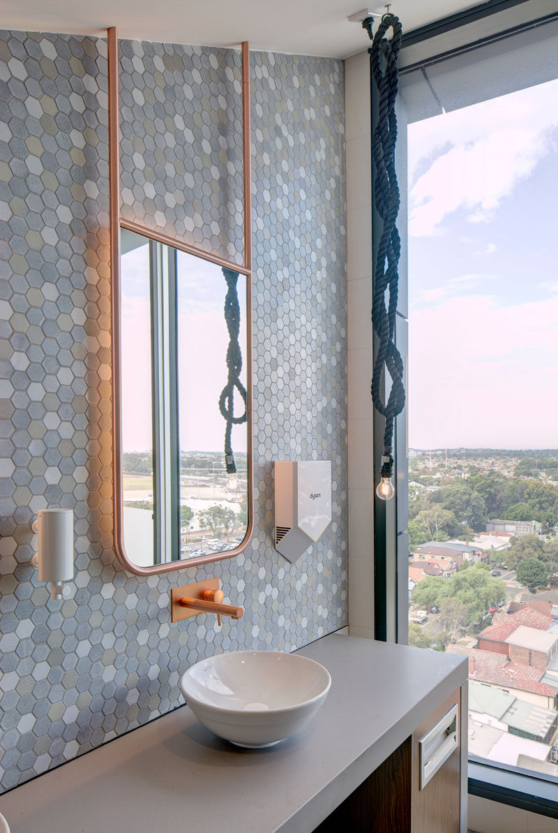 This modern bathroom has soft multi-colored hexagonal tiles as a accent wall, and a backlit copper framed mirror that hangs from the ceiling. #Bathroom #ModernBathroom