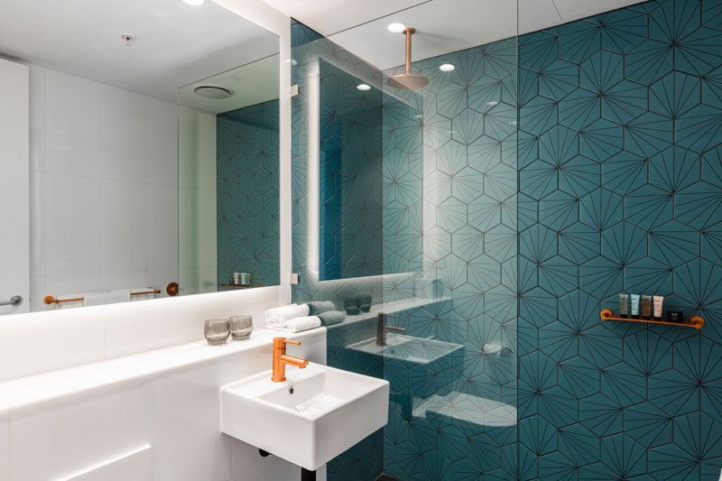 This modern bathroom features a dark turquoise, patterned accent wall in the shower, while a backlit mirror helps to keep the space bright. #Bathroom #AccentTile