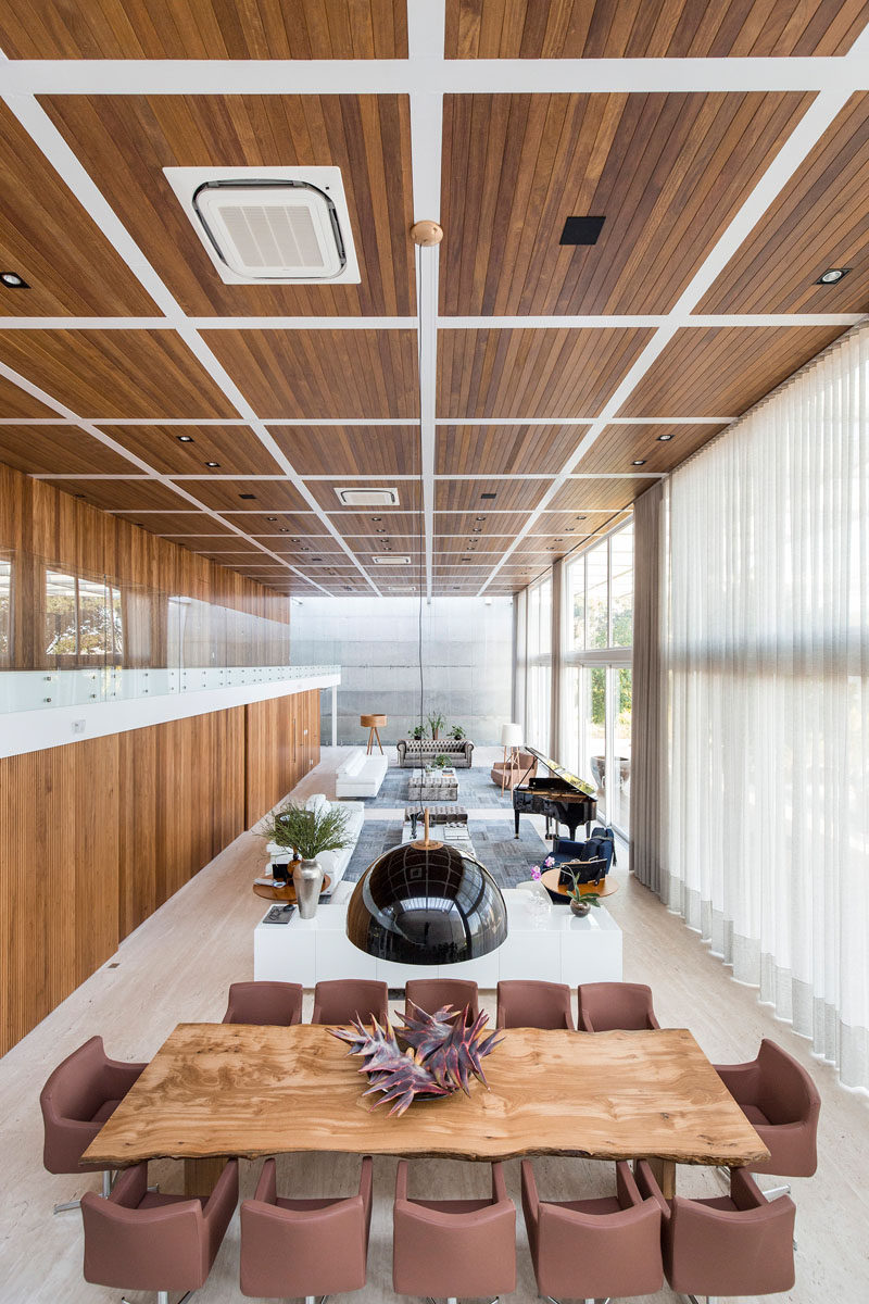 This modern house has a large double height living room and dining room. The kitchen and a home theater are hidden behind sliding wood doors. #LivingRoom #ModernInterior