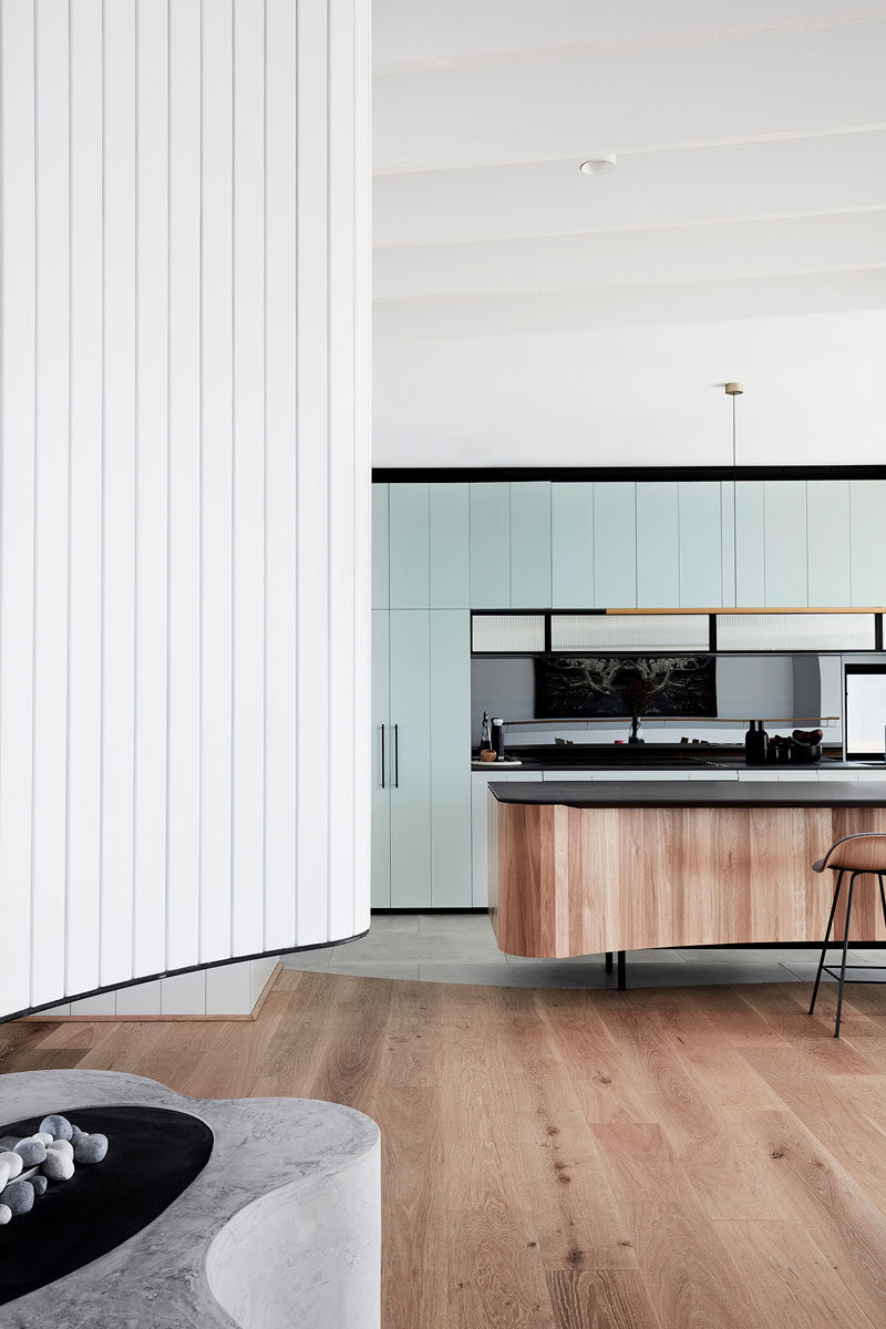 In this modern kitchen, light blue cabinetry by Building With Options has been combined with a reconstituted stone benchtop and an island covered with vertical wood pieces. #ModernKitchen