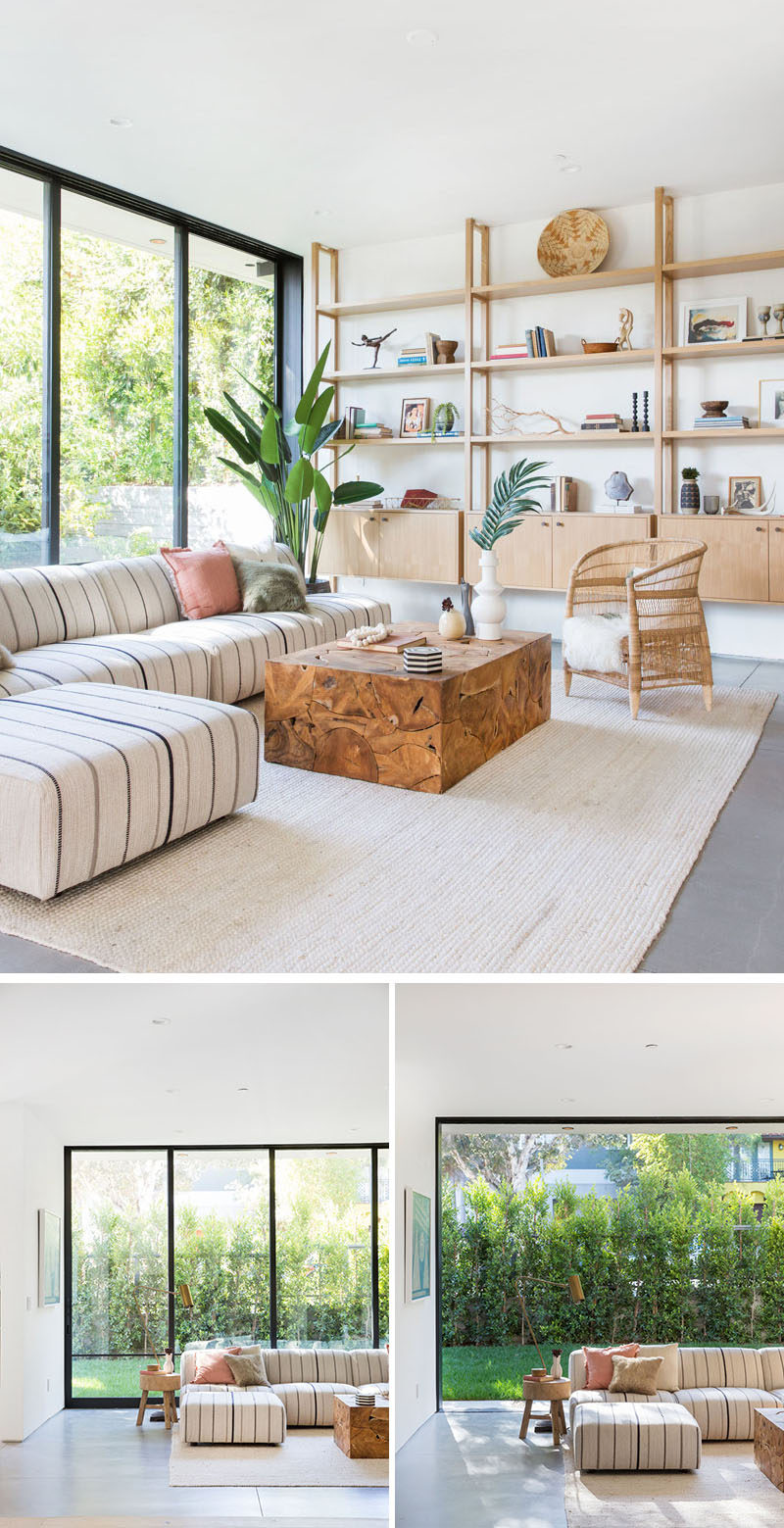 This contemporary living room features a wall of light wood shelving, while floor-to-ceiling sliding glass wall floods the interior with natural light. #LivingRoom #Shelving #SlidingGlassWall