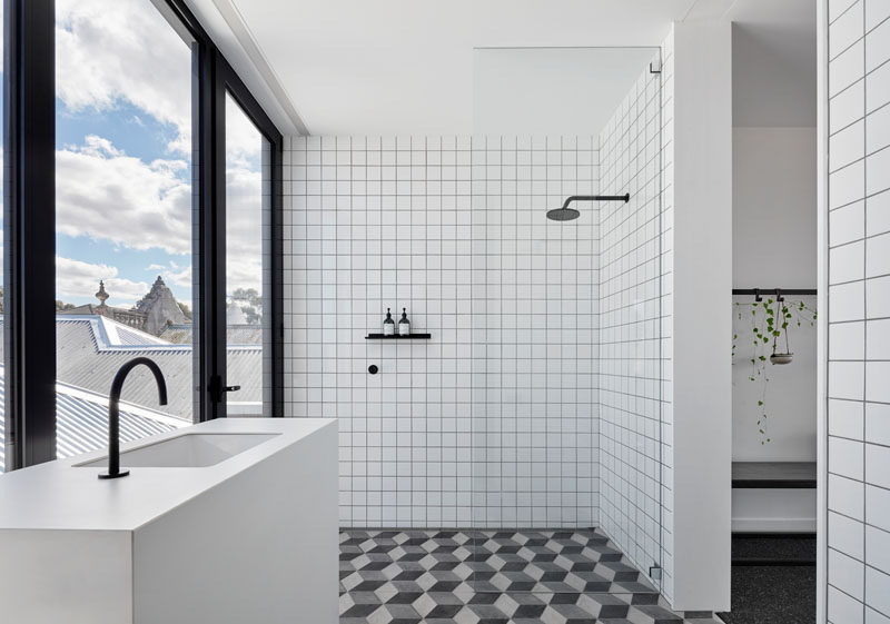 This bathroom features Marca Corona hexagonal tiles on the floor, and simple white square tiles with a dark grout on the walls. Matte black bathroom fixtures complement the window frames and create a modern appearance. #ModernBathroom #BathroomDesign