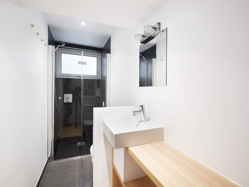 This small bathroom has a glass enclosed shower with dark tiles, and a small partition wall separating the vanity area from the toilet. #SmallBathroom #BathroomDesign