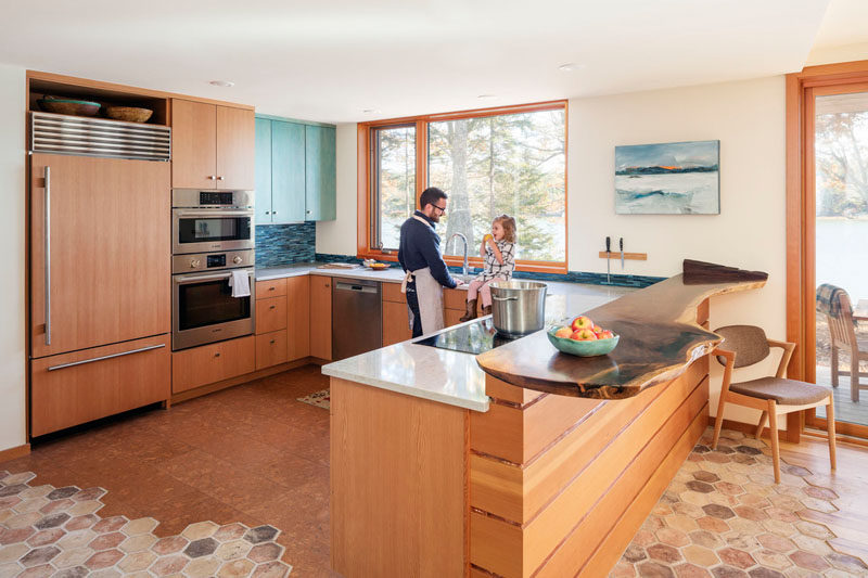 In this U-shaped kitchen, a live edge bar sits next to the countertops, while beside the kitchen are doors that lead to the deck with water views. #WoodKitchen #KitchenDesign