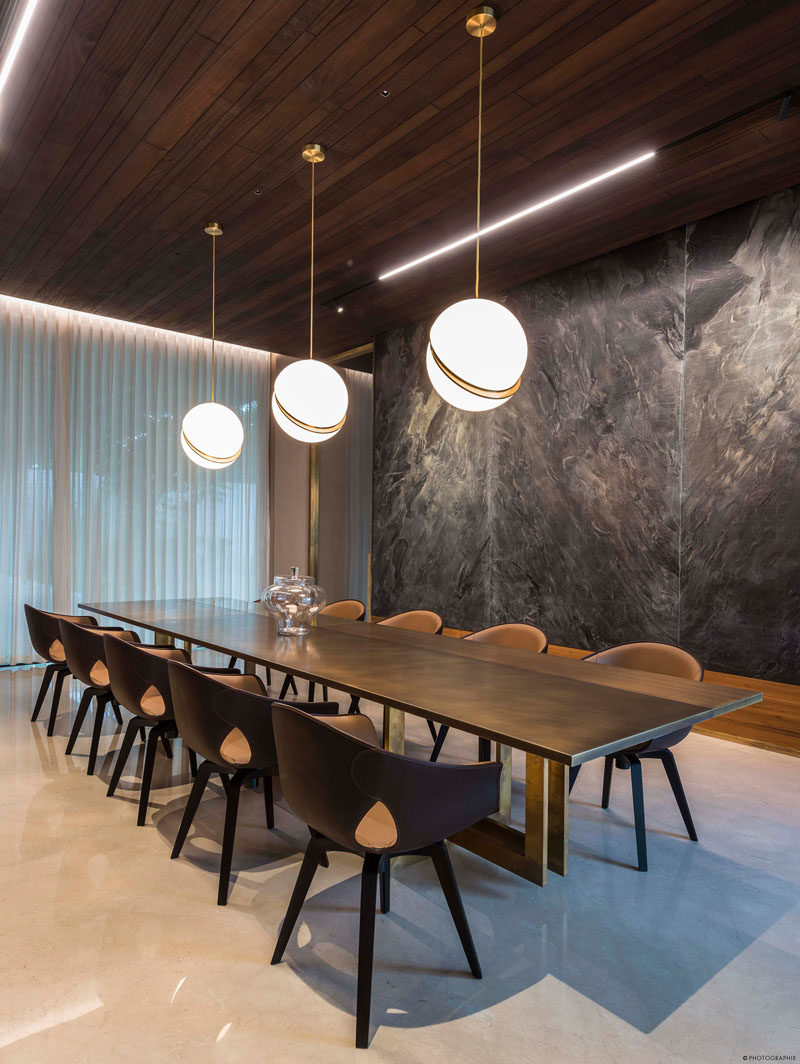 In this modern dining room, three pendant lights hang above a large dining table, while stone slabs are featured on the wall. #DiningRoom #LargeDiningTable
