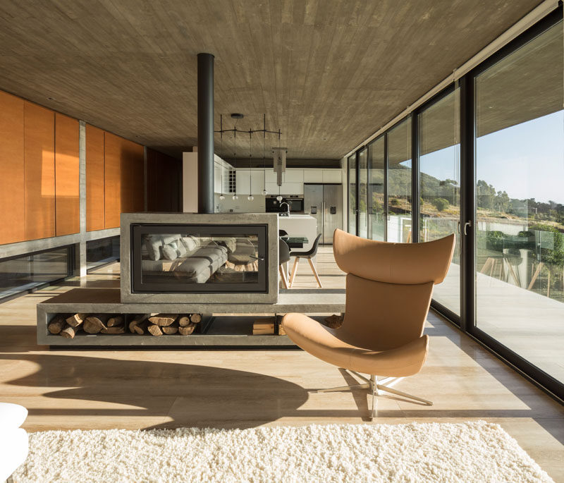 The living room and dining area in this modern concrete house share a double-sided fireplace that provides warmth and separation in the open plan room. Click through to see more photos of this house. #Fireplace #FirewoodStorage #InteriorDesign