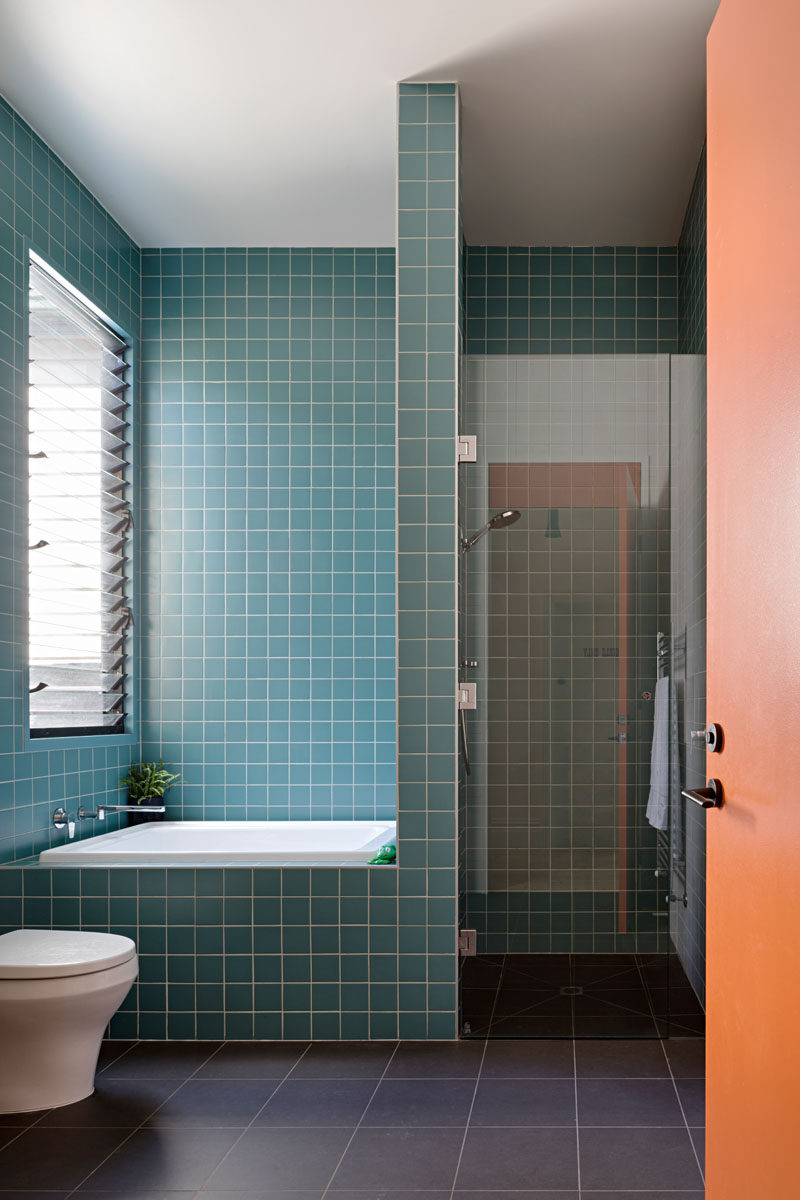 In this modern bathroom, there's a walk-in shower and a half-size bath that are surrounded by square blue tiles with a white grout. #BathroomDesign #SmallBathtub #ModernBathroom #BlueTiles