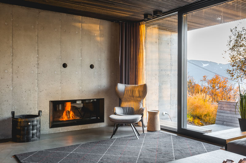 This modern living room has a concrete wall with a built-in fireplace, and a large sliding glass door opens to the outdoors. #ModernFireplace