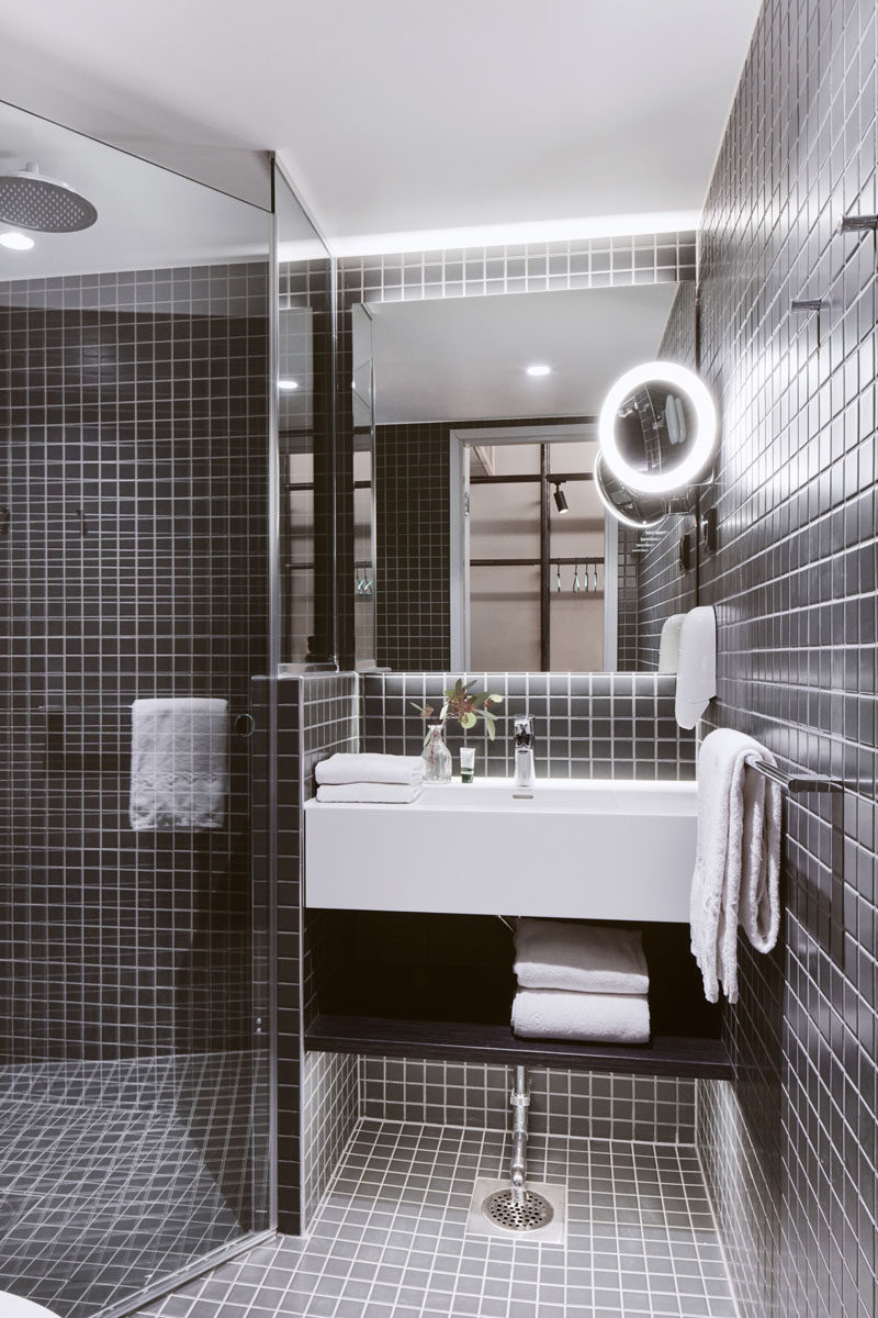 This modern hotel bathroom has dark tiles that contrast the bright white vanity. #ModernBathroom #DarkTiles