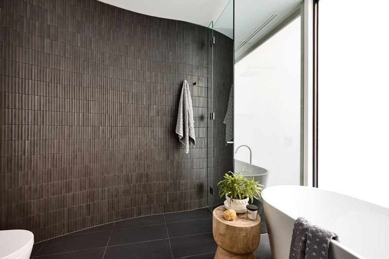 This modern bathroom features a curved brown-tiled wall that continues through into the shower, that's somewhat hidden behind a mirror. Click through to see more photos of this modern house. #ModernBathroom #BrownTiles #BathroomDesign