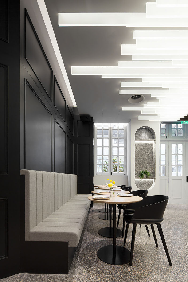 This bar area within a restaurant has black accent walls that match the black chairs, and dramatic lamella lighting on the ceiling. #RestaurantDesign #Lighting