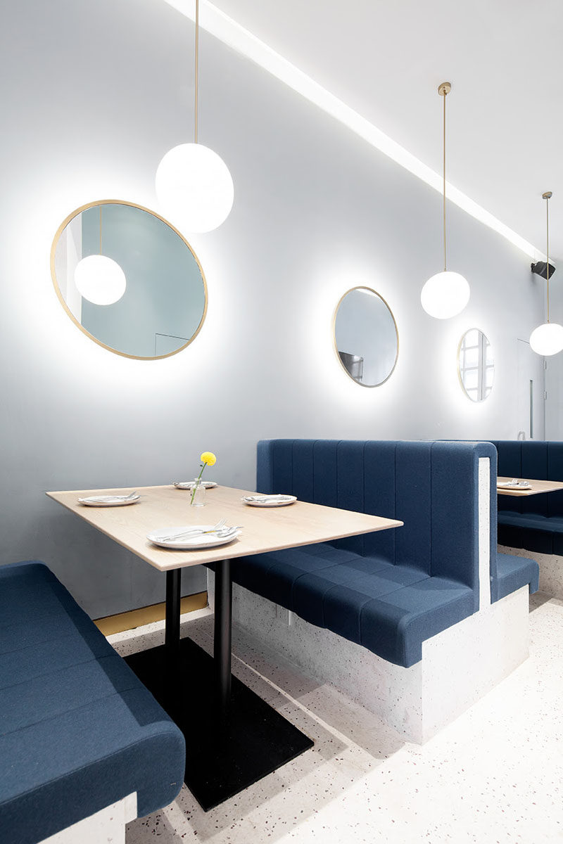 This modern restaurant booth seating with blue upholstery and round backlit mirrors on the wall. #ModernRestaurant #BoothSeating