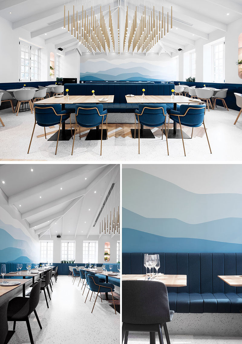 This modern restaurant has a pitched ceiling that's highlighted by striking brass installation that hangs above the space and a calming mountain mural in blues and greys. #ModernRestaurant #OmbreWall