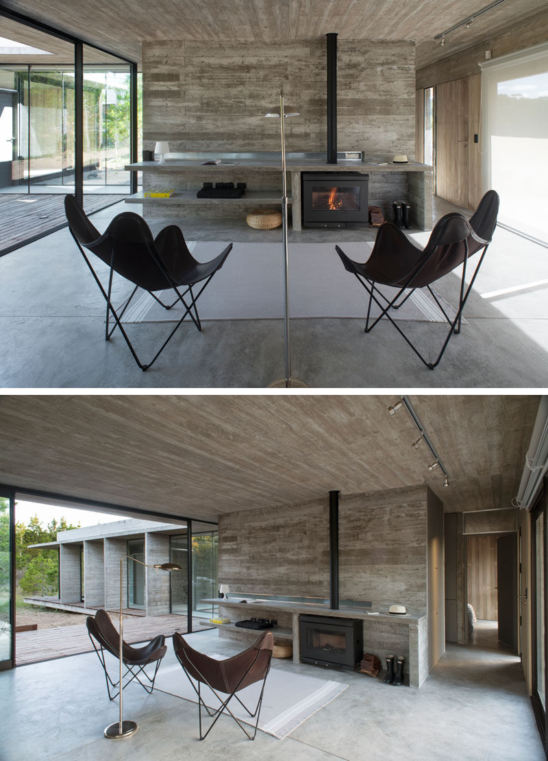 Inside this modern house, board formed concrete has been used for the walls, ceiling and shelving elements, while large floor-to-ceiling windows and sliding glass doors allow natural light to flood the interior of the home. #BoardFormedConcrete #Fireplace #LivingRoom