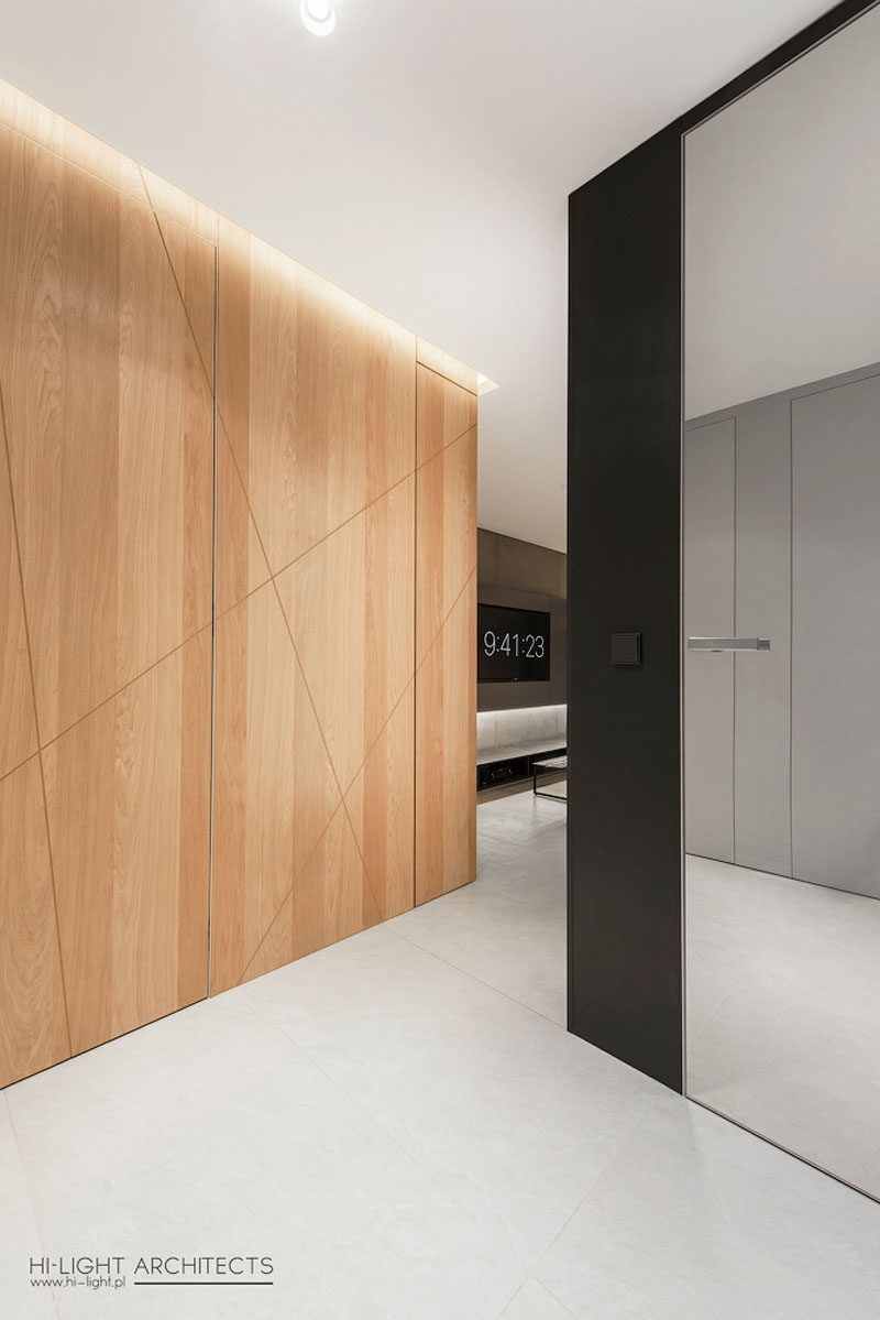 Stepping inside this modern apartment, the front door almost blends away into the wood accent wall with hidden lighting, while a black box leads into the living room. #WoodAccentWall