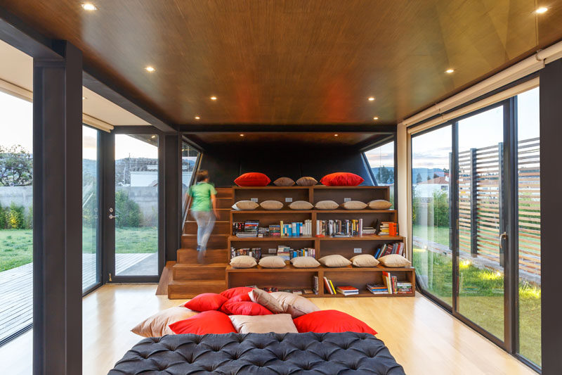 This modern house has a reading area with stairs and stadium seating. The wood stadium seating has open fronts for storing books and pillows. #HomeLibrary #Seating #InteriorDesign