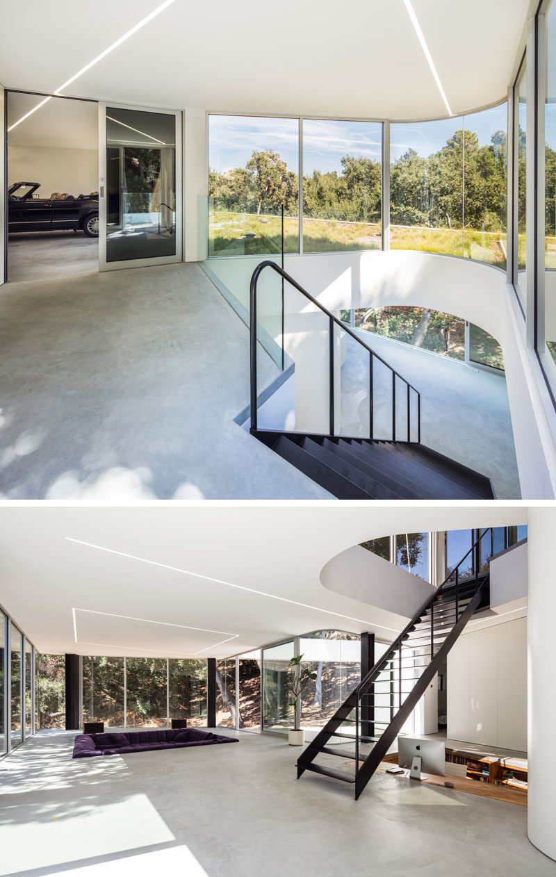 Next to the garage in this modern house, are stairs that lead down to the living level of the house, and sunlight from the curved windows is able to funnel down through the stairwell. #BlackStairs #CurvedWindow