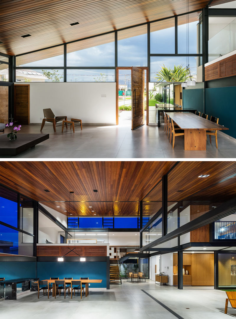 A pivoting wood front door welcomes visitors to this modern house, and once inside, there's a pop of blue in the dining area that contrasts the large wood ceiling and concrete floor. #ModernHouse #WoodCeiling #DiningTable