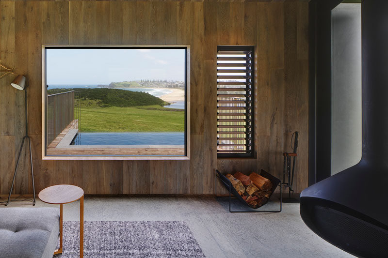 This modern guest house living room has a fireplace that hangs from the ceiling, while a window looks out onto a small pool. Click through to see more photos of the guest house. #Window #Fireplace #WoodWalls