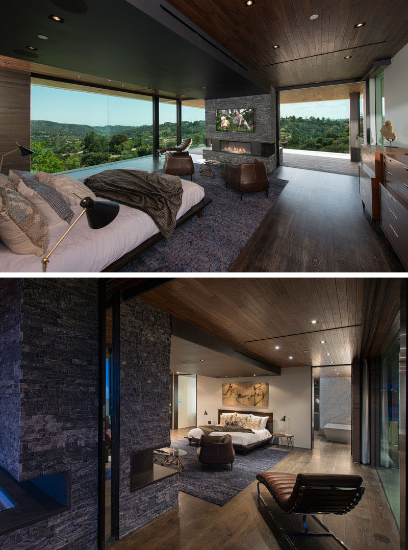 This modern master bedroom suite has an indoor/outdoor gray, stacked-stone fireplace that also heats the terrace outside. The ceiling features solid walnut planks, while the flooring is custom stained 10-inch oak flooring. #MasterBedroom #Fireplace