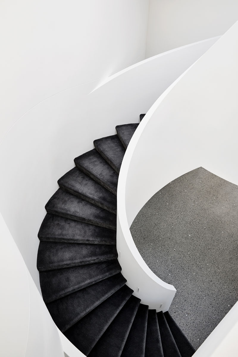 Black stair treads strongly contrast the white spiral staircase. Click through to see more photos of this modern house. #SpiralStairs #BlackAndWhite #Stairs #Staircase #BlackStairTreads