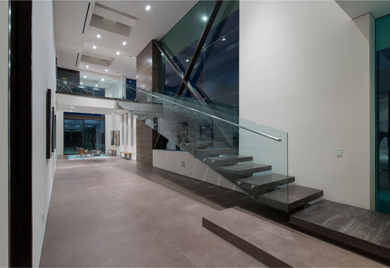 Stairs with a glass and metal handrail follow the wall and lead up to the second floor of this modern home. #ModernStairs