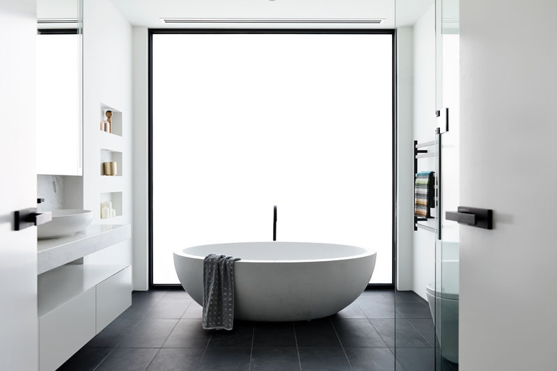 In this modern bathroom, a frosted window becomes the backdrop for the freestanding bathtub. Click through to see more photos of this modern house. #ModernBathroom #FrostedWindow #FreestandingBathtub #BuiltInShelving