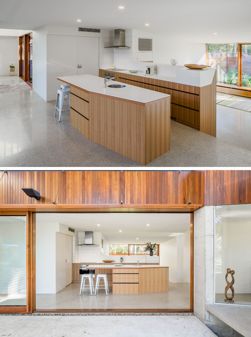 This modern kitchen has bright white countertops and light wood cabinetry. A large sliding door opens the kitchen to a covered outdoor space. Click through to see more photos of this modern house. #KitchenDesign #KitchenLayout #ModernKitchen #WoodAndWhiteKitchen