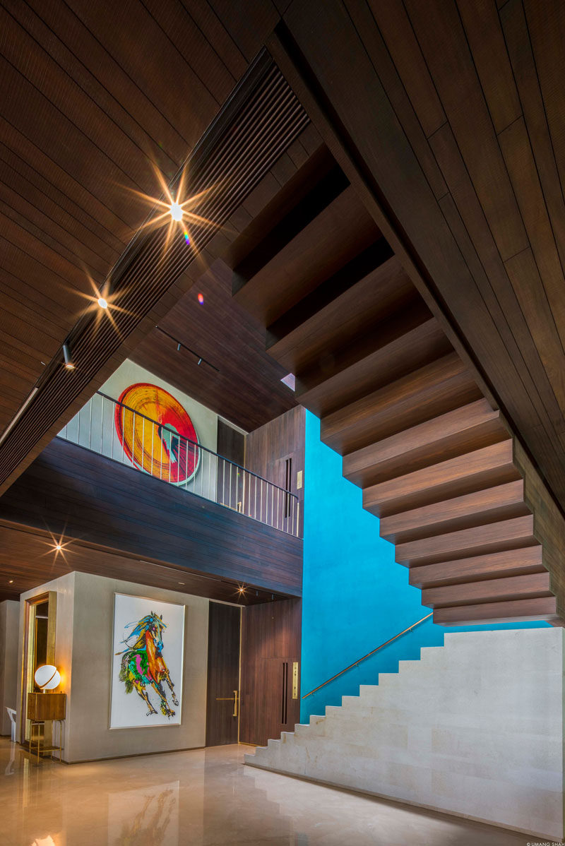 Throughout this modern house rich dark wood has been paired with rendered lime plaster walls with a stucco-like appearance. Pops of color, like the blue accent wall next to some stairs, add a touch of brightness to the interior. #InteriorDesign #WoodCeiling #Stairs