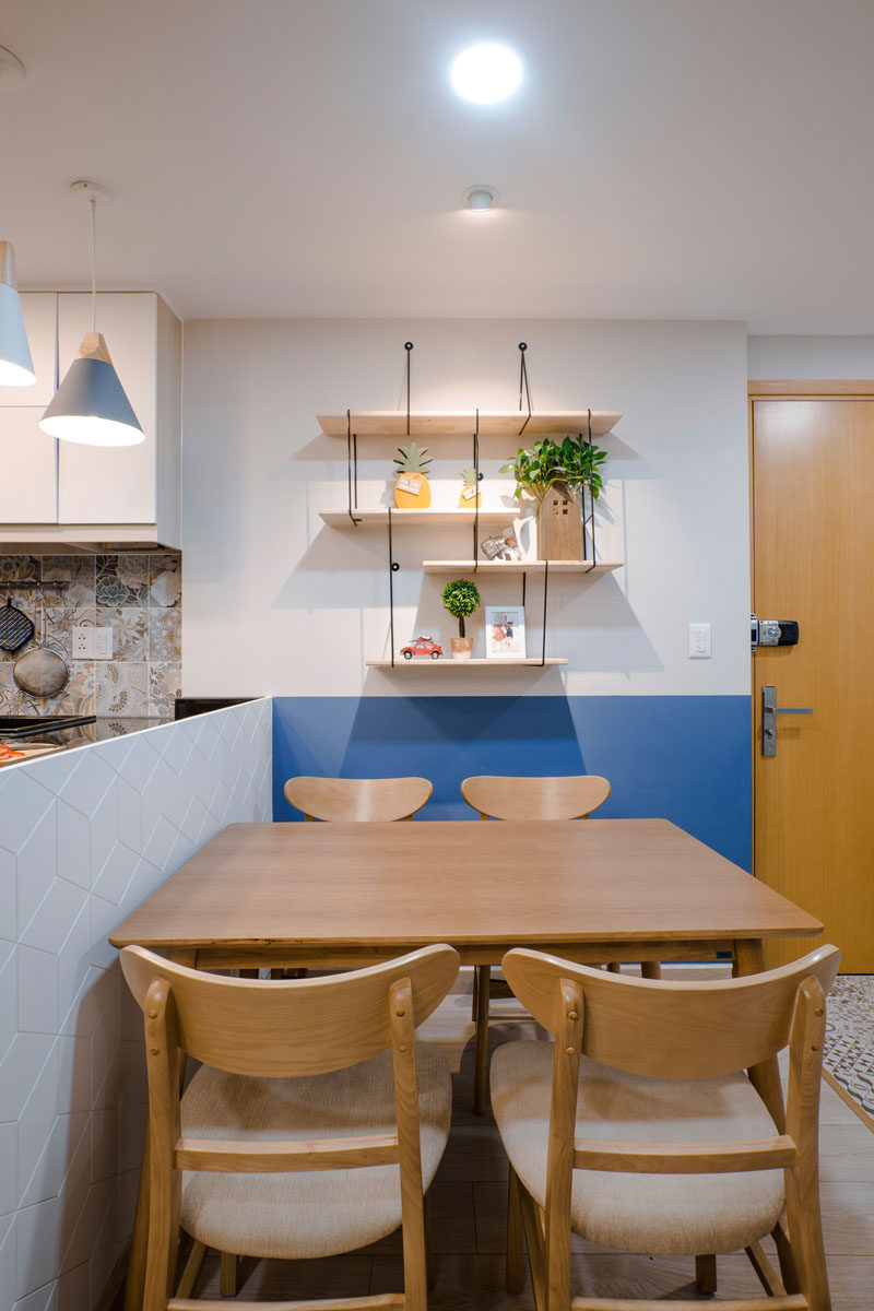 Wood shelves, decorated with plants and personal items, hang on the wall of this dining area, while a blue section of wall matches up with the line of the kitchen. Click through to see more photos of this apartment. #DiningRoom #HangingShelves