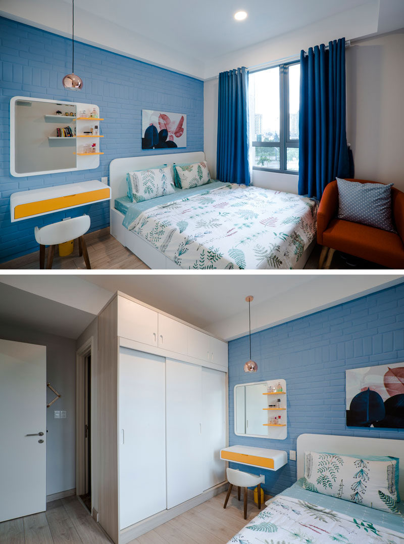 In this modern bedroom, a soft blue accent wall creates a relaxing environment, while a pop of yellow in the small vanity and shelves adds a cheerful touch. Click through to see more photos of this apartment. #BlueAccentWall #BedroomDesign #Bedroom #BedroomIdeas
