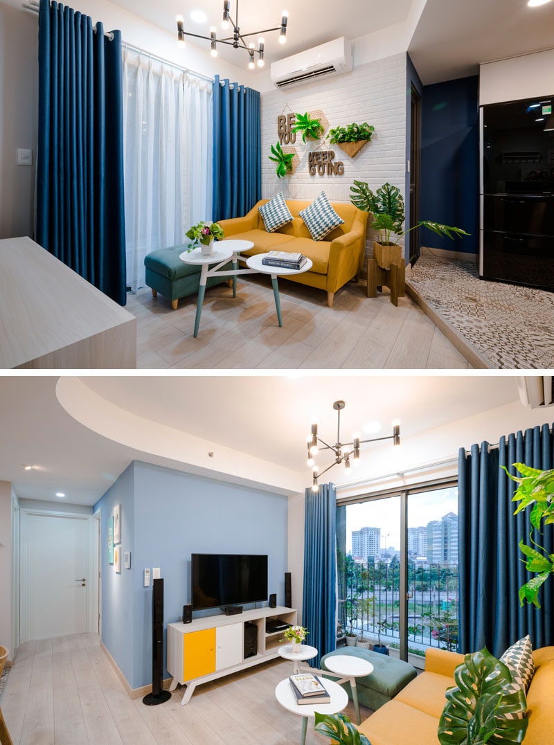 In this living room, a warm yellow sofa has been paired with a painted white brick wall, bright green plants and blue curtains for a contemporary look. Click through to see more photos of this apartment. #BlueAndYellow #LivingRoom #InteriorDesign #SmallLivingRoom