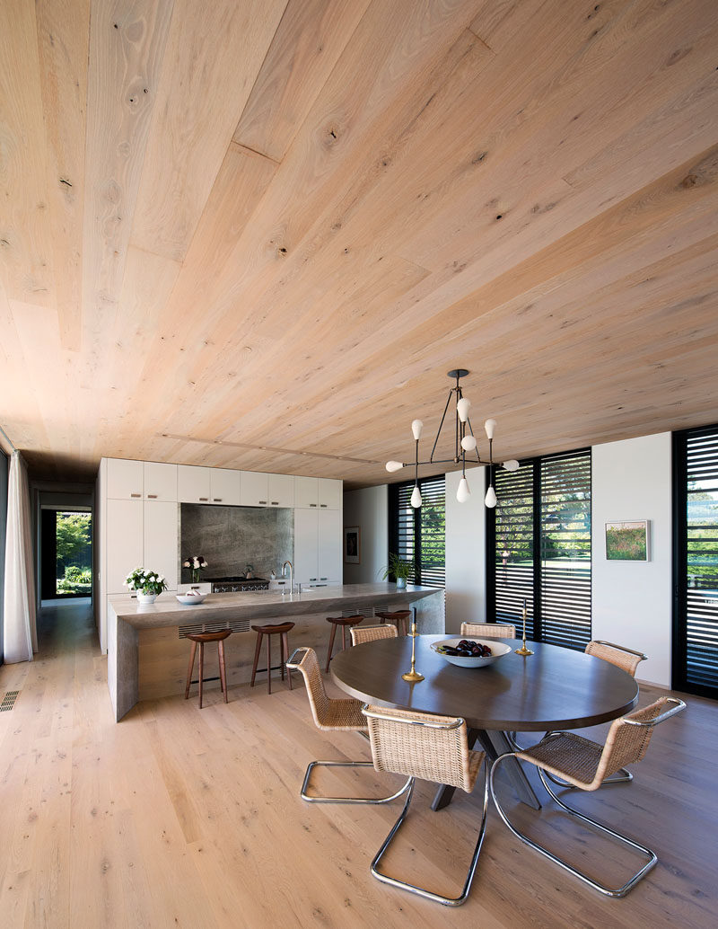 This modern kitchen, with white cabinets and a large island, shares the room with a casual dining area with a round table and a minimalist chandelier. #ContemporaryInterior #KitchenDesign #RoundDiningTable