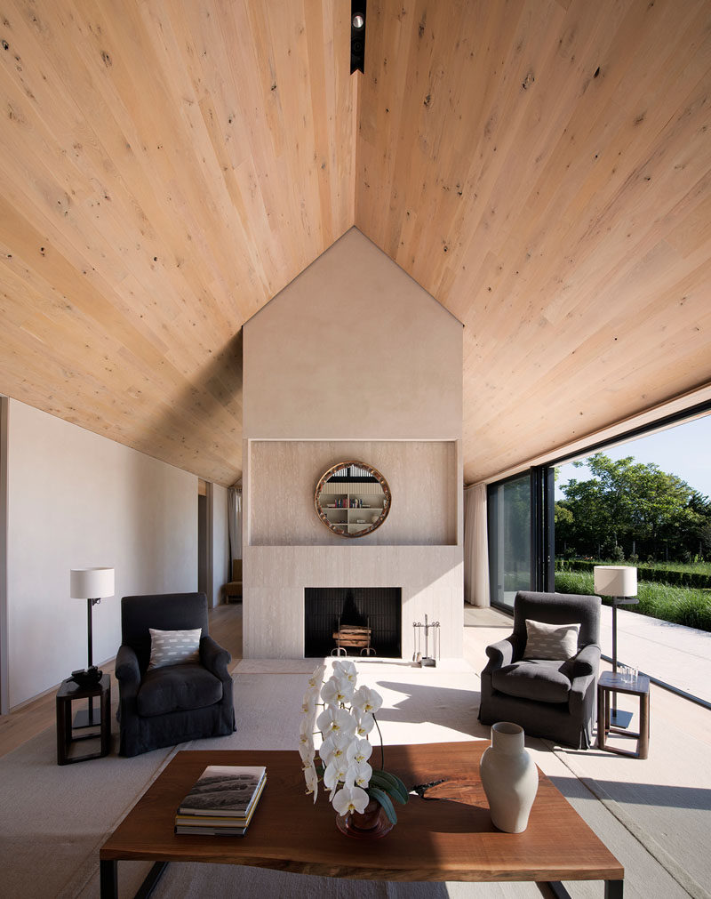 Inside this modern house, wood covers the ceiling and oak has been used for the floor, while sliding glass doors open the interior spaces to the patio outside. #ContemporaryLivingRoom #WoodCeiling #Fireplace #InteriorDesign