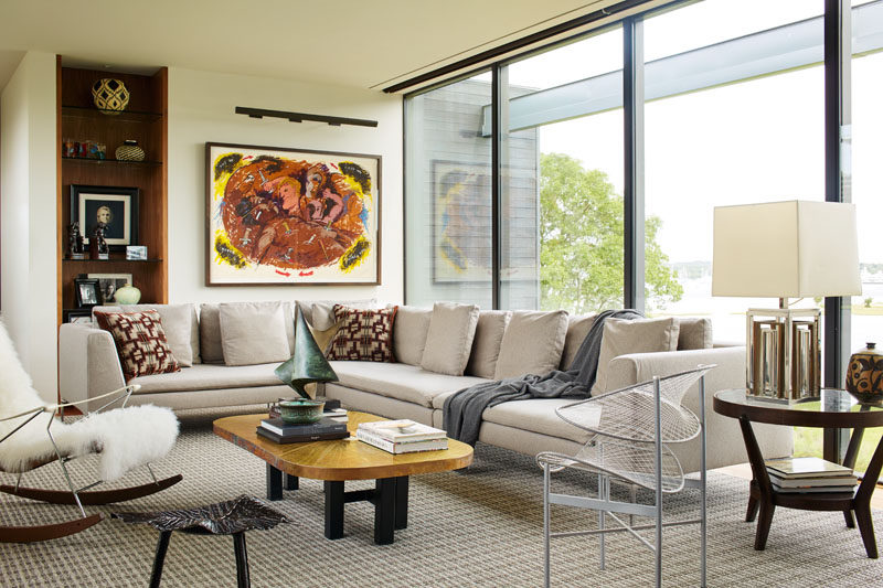 In this family TV room, simple light colored furnishings create a contemporary room, while a built-in floor to ceiling shelf has been lined with wood. #ContemporaryLivingRoom #Shelving