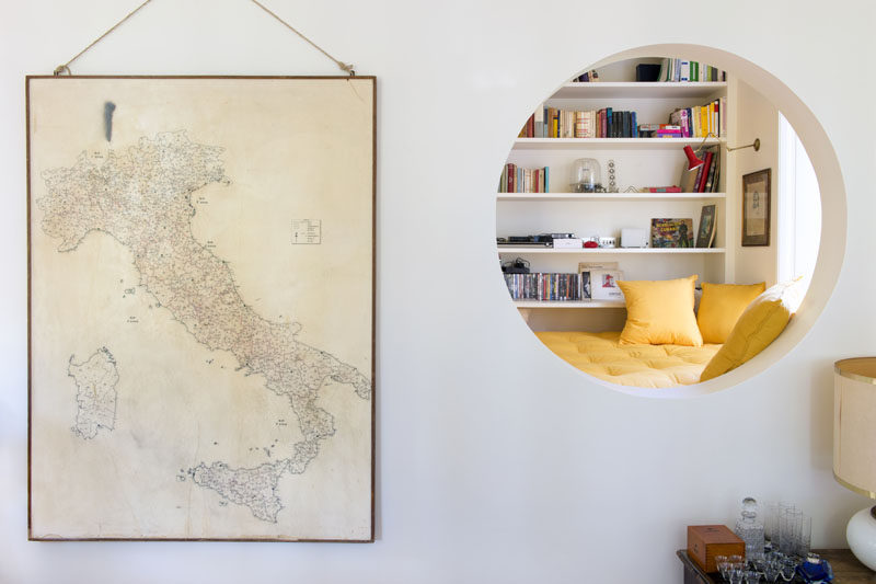 This modern home features an elevated reading nook that sits next to a window and a floor-to-ceiling bookshelf, and that has an opening that looks into the living room. #ReadingNook #InteriorDesign #CozyNook #Nook