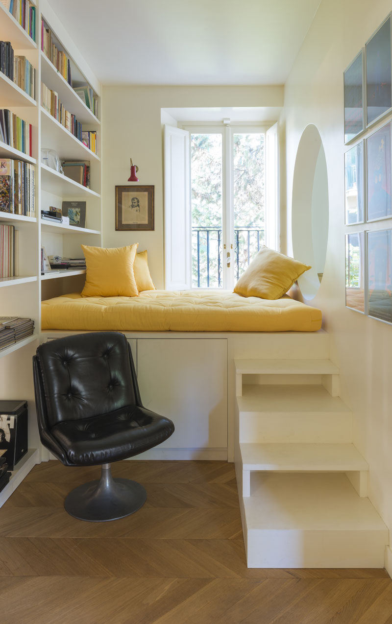 This modern home features an elevated reading nook that sits next to a window and a floor-to-ceiling bookshelf, and that has an opening that looks into the living room. #ReadingNook #InteriorDesign #CozyNook #Nook