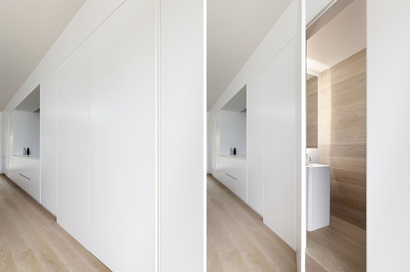 The streamlined minimalist white kitchen cabinets line the wall in this modern house, and hidden behind one door is a powder room. #HiddenPowderRoom #KitchenDesign #WhiteCabinets