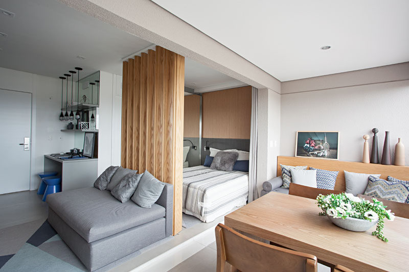 The modern living and sleeping areas of this small apartment open up to an integrated balcony that has a living area, dining area and laundry space. #SmallApartment #InteriorDesign #IntegratedBalcony #WoodSlatPartition #WoodSlatWall