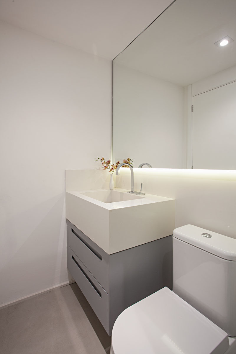 The bathroom has been kept minimalist with a simple grey and white vanity. Hidden lighting under the mirror creates added light in the small space. #SmallBathroom #ModernBathroom