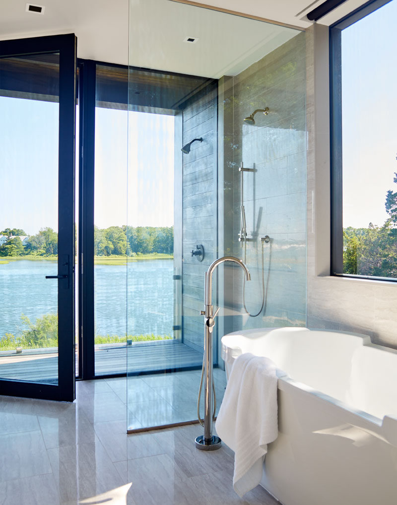 This modern bathroom has floor-to-ceiling windows and glass door that opens to a small balcony. #ModernBathroom #BathroomDesign