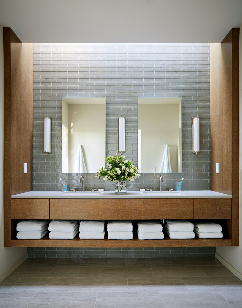 In this modern bathroom, grey tiles have been combined with wood cabinetry that has an open shelf for towel storage. #BathroomDesign #ModernBathroom #WoodVanity #GreyTiles