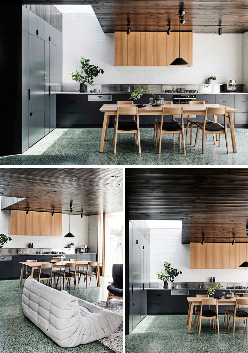 In this modern kitchen, appliances like the fridge are hidden in plain sight within the dark cabinets, and a stainless steel backsplash helps to reflect light. #ModernKitchen #KitchenDesign #InteriorDesign