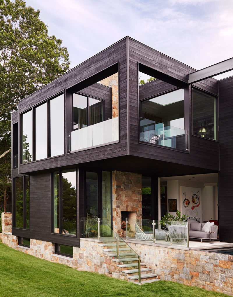 This modern house has a small outdoor lounge with a fireplace and steps that lead down to the lawn. #OutdoorLounge #OutdoorFireplace #Stone