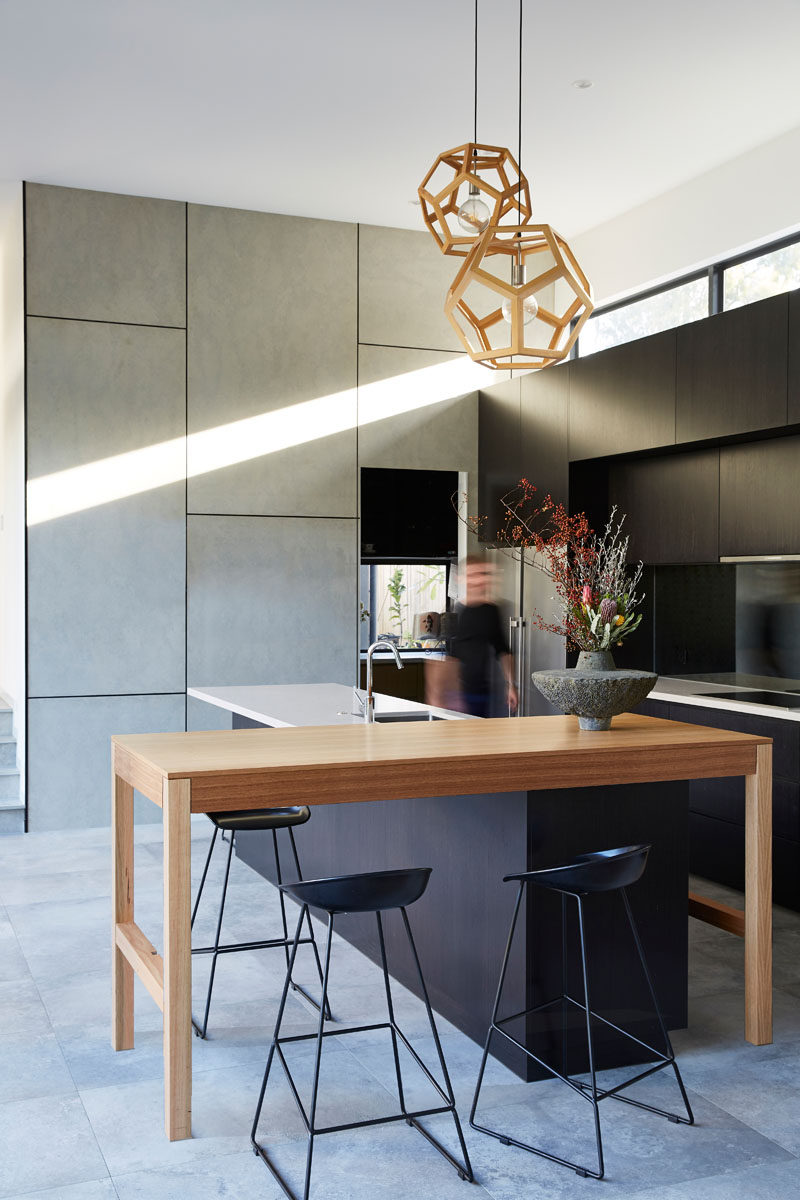 In this modern kitchen, black cabinets have been combined with wood elements and white countertops. #ModernKitchen #KitchenDesign