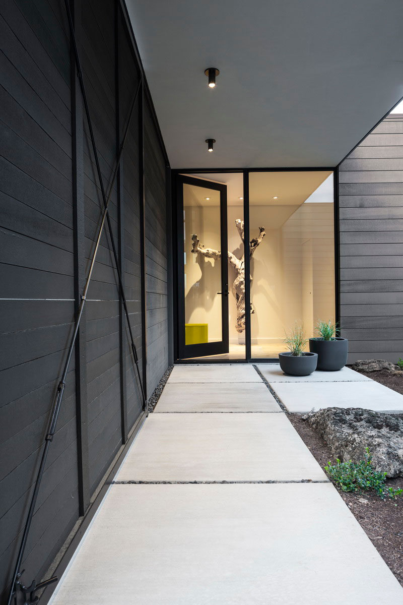 At the entry courtyard of this modern house, a rolling screen and swinging gate can be configured to be cozy and private, or wide open and welcoming.  #ModernHouse #GlassDoor #ConcretePath